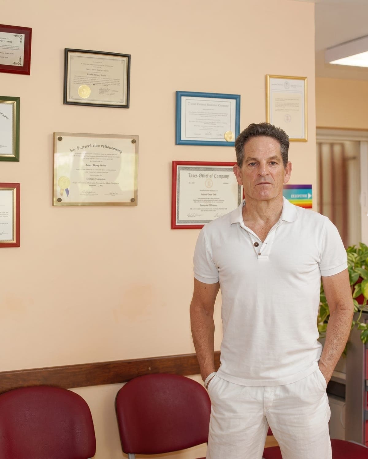 El Dr. Randall Jones, de pie ante la pared donde cuelgan sus titulaciones enmarcadas.